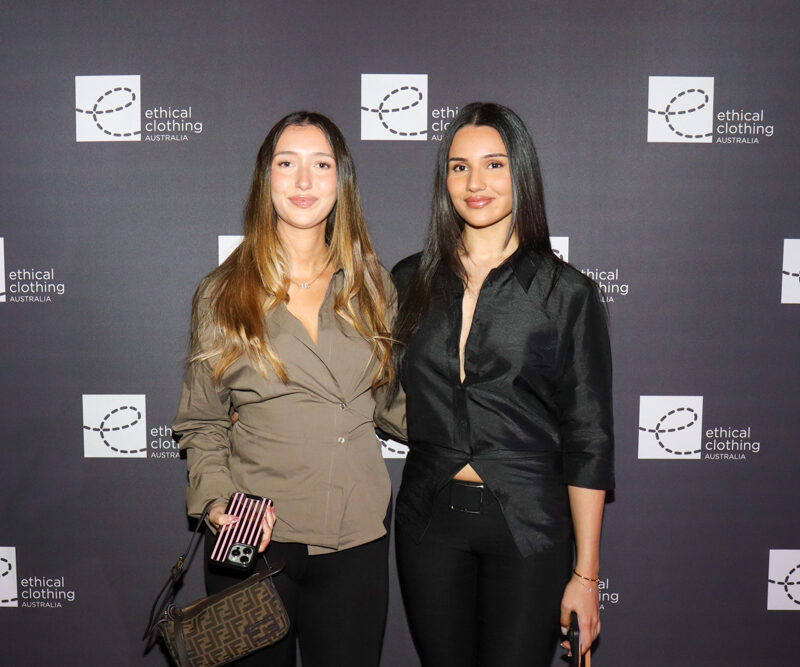 Two women standing in from of black media wall with a white e symbolising the Ethical Clothing Australia logo.