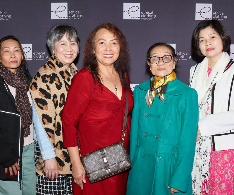 Five women standing in from of black media wall with a white e symbolising the Ethical Clothing Australia logo.